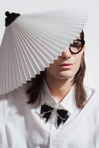 A stylish person in glasses with creative fashion sense, wearing a lampshade hat indoors.
