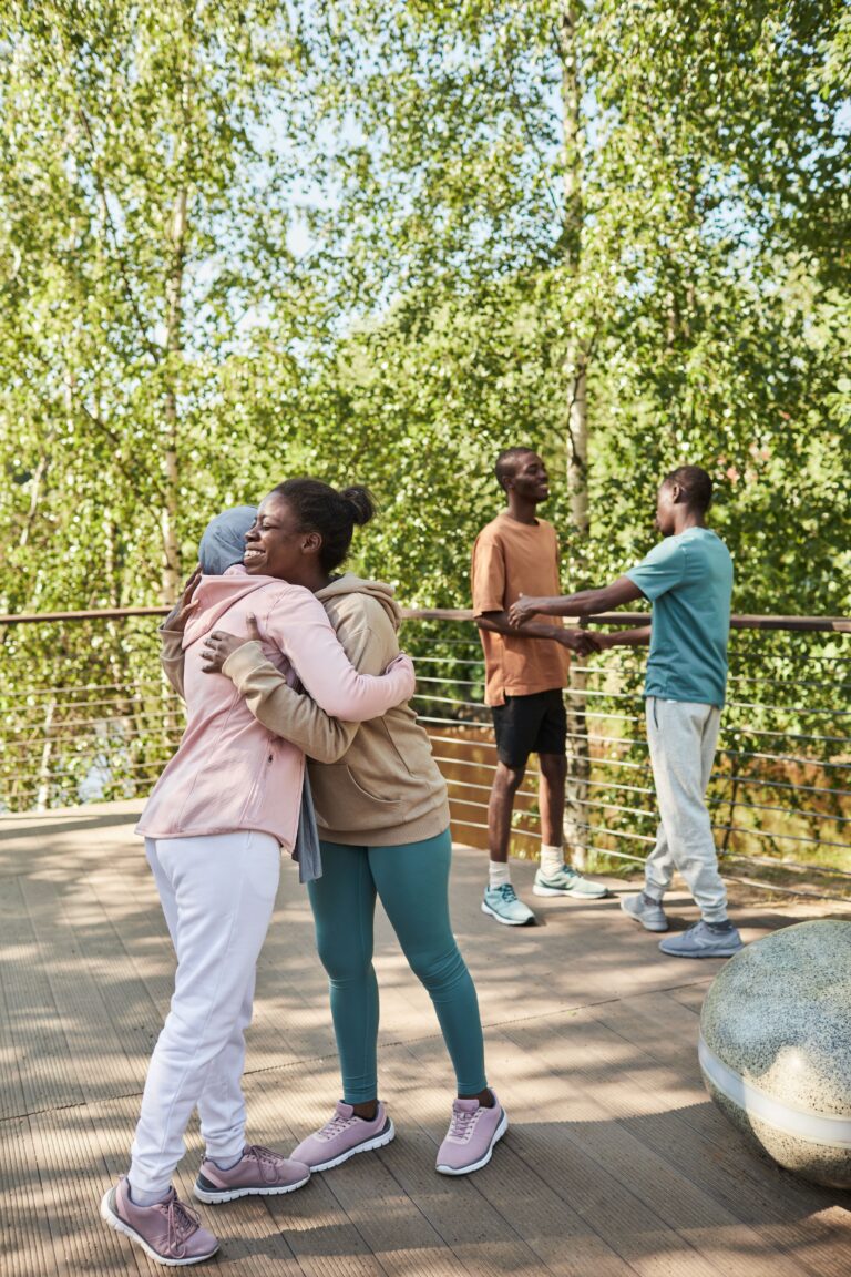 A joyful group of friends hugging and chatting outdoors in a sunny park setting, enjoying the summer weather.